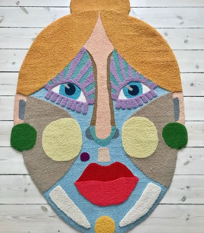 Large colorful tufted face rug displayed on a wooden floor by Ina Dyreborg