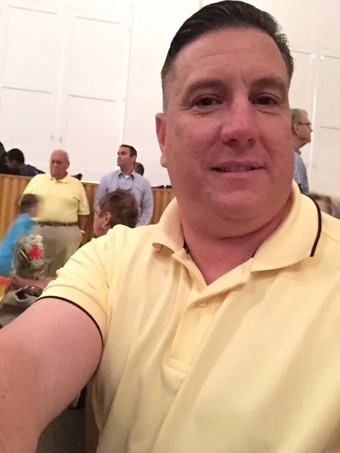 Man in a yellow polo taking a selfie with funny background hijacks the moment.
