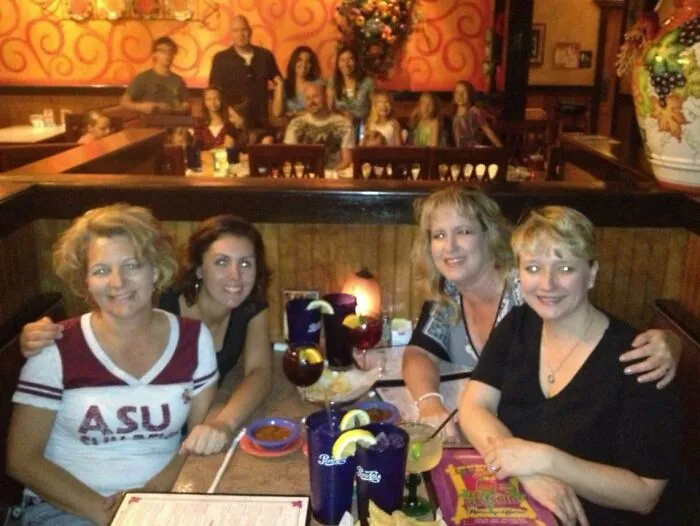 Four women dining in a restaurant with another large family in the background