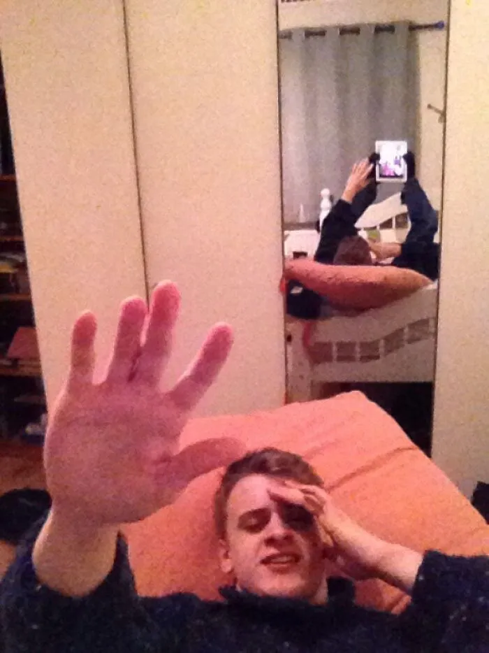 A man holding his hand up with a funny reflection in the background mirror