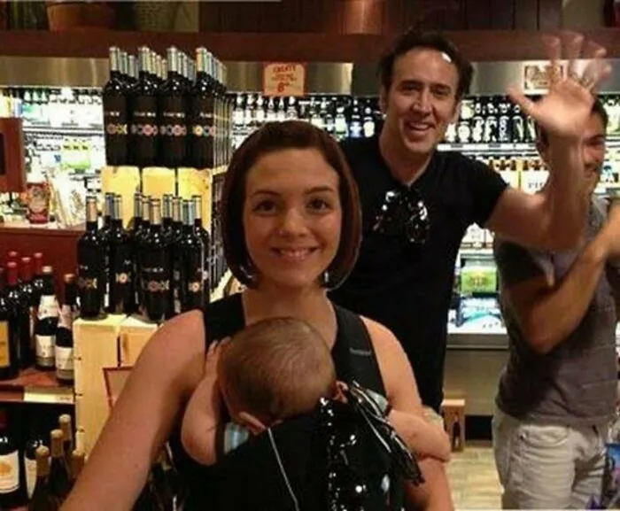 Nicolas Cage in the background photobombs a mother holding her baby in a store