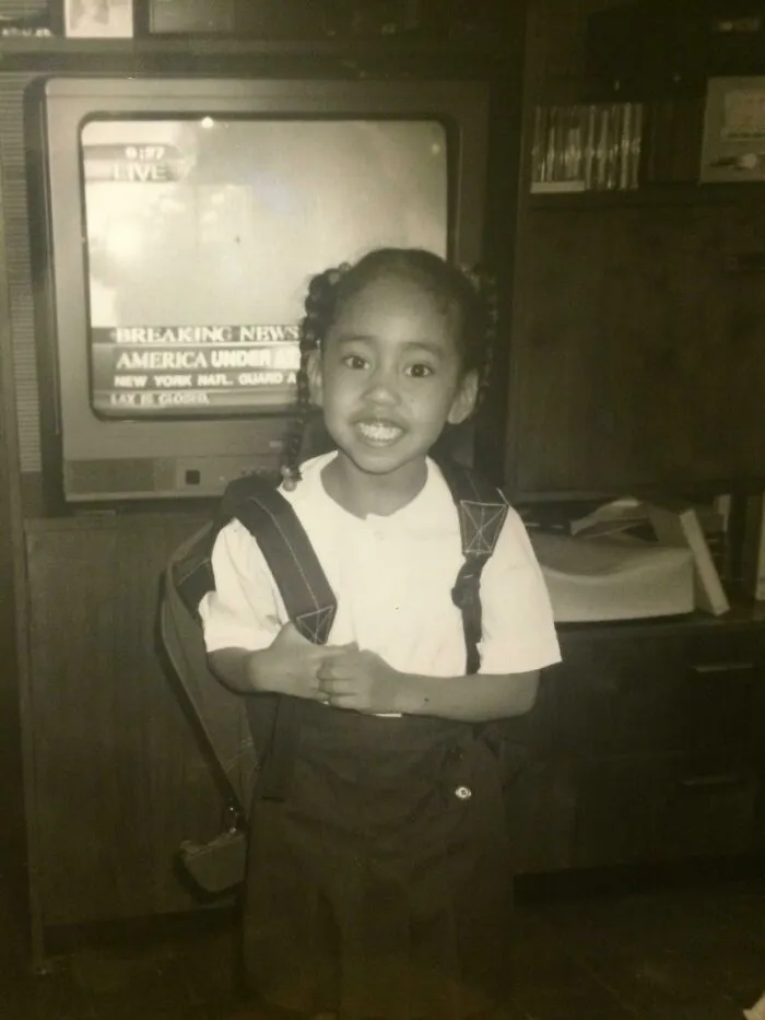 A young girl in school uniform smiles as breaking news displays in the background