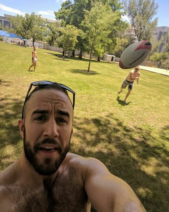 Bearded man selfies while a football in the background hijacks the moment.