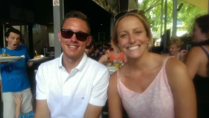 A photobomb of a server making a funny face in the background of a couple sitting at a restaurant.