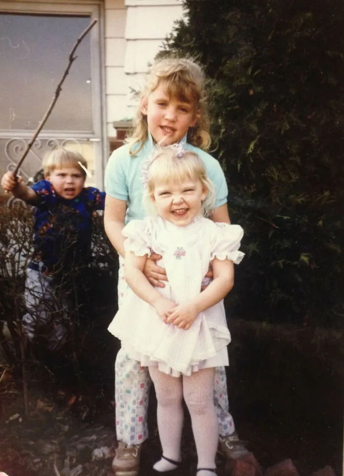 Two girls pose for a picture while a boy with a stick in the background completely hijacked the moment.