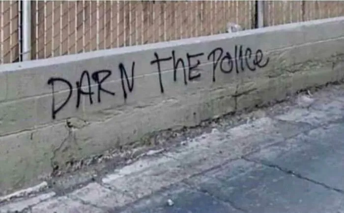 Vandalism on a concrete wall with black spray paint reading Darn the Police as a polite act of public art