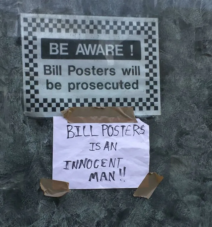 A hand-written note under a warning sign claiming Bill Posters is an innocent man as a humorous act of vandalism