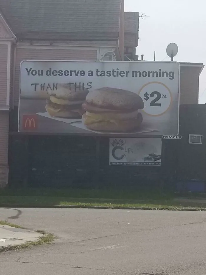 Clever vandalism on a fast food breakfast billboard adding humorous graffiti critique