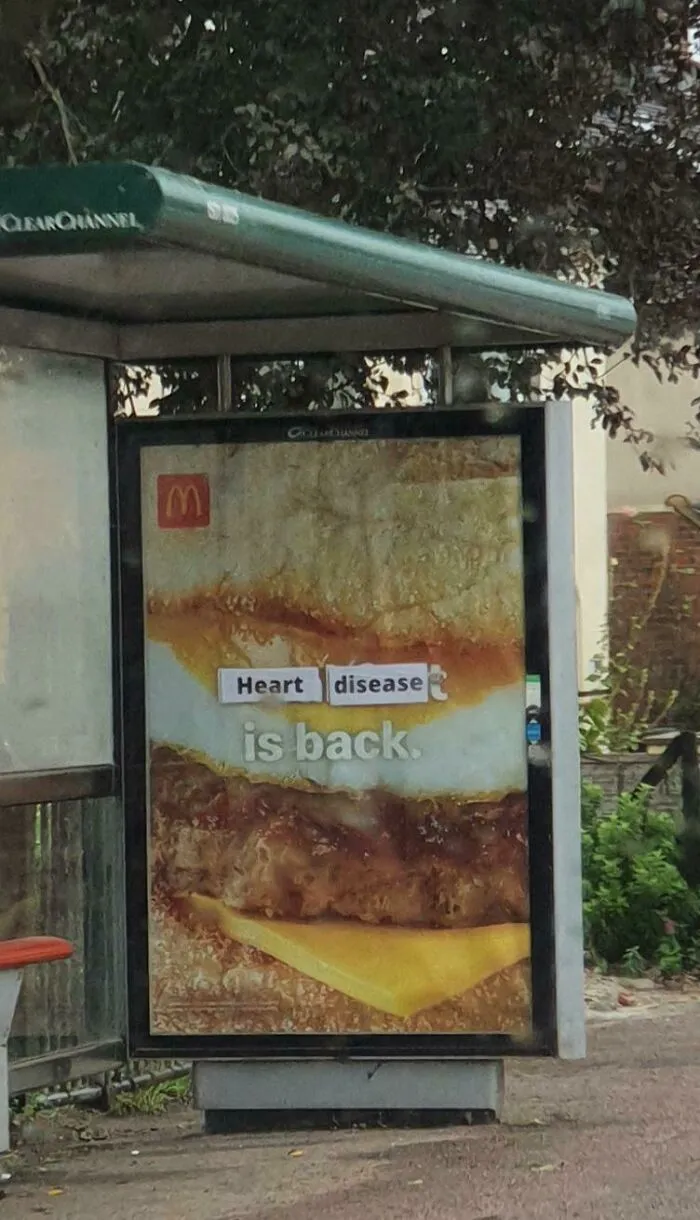 A bus stop fast food ad stickered to read Heart disease is back, showing a clever act of vandalism as public art.