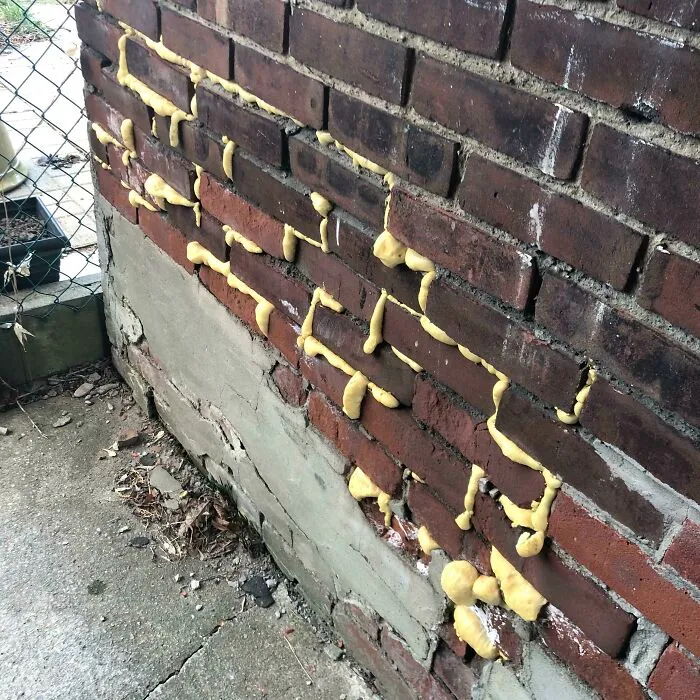 A brick wall messily patched with yellow expanding foam, demonstrating a botched home renovation job.
