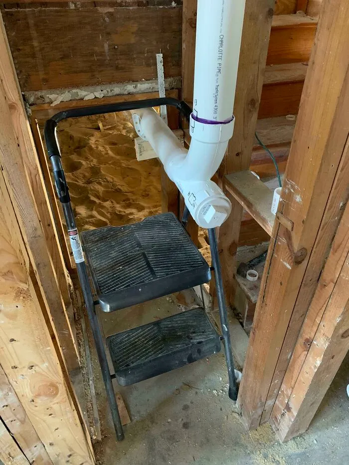A white PVC pipe oddly routed through a black step ladder, showing a complete fiasco in home renovation.