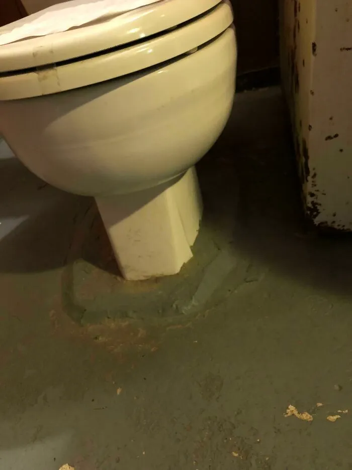 A poorly installed toilet sealed with a thick ring of gray cement, a complete fiasco of a bathroom repair.