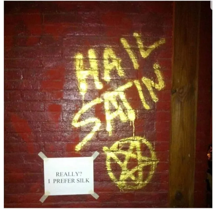 A gold spray-painted pentagram on a red brick wall with a funny response sign, an act of vandalism as public art.