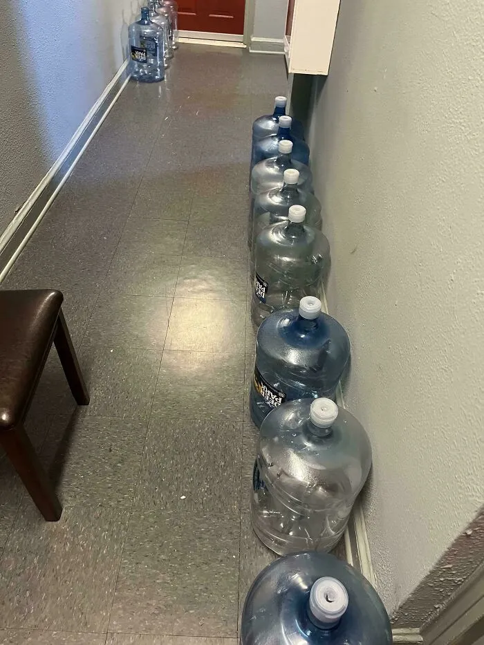 A row of large water jug delivery bottles blocking a shared apartment hallway from infuriating neighbors