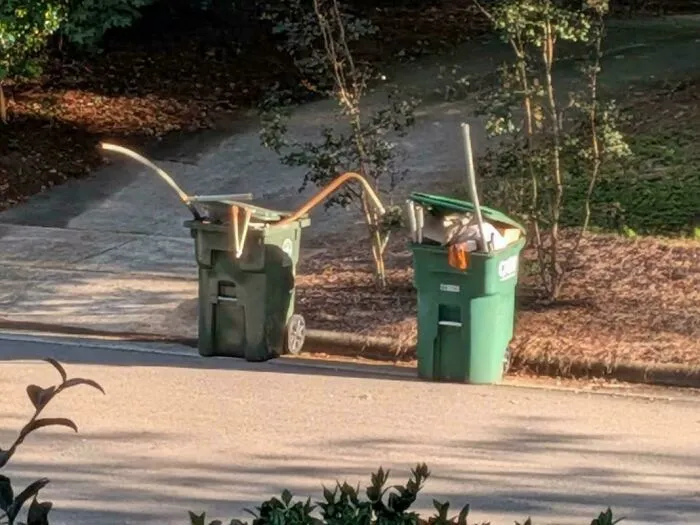 Overfilled trash cans placed on the curb by infuriating neighbors causing a mess along the street.