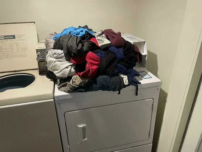 A pile of clothes left on top of a shared washing machine showing infuriating neighbors habits in an apartment laundry room.