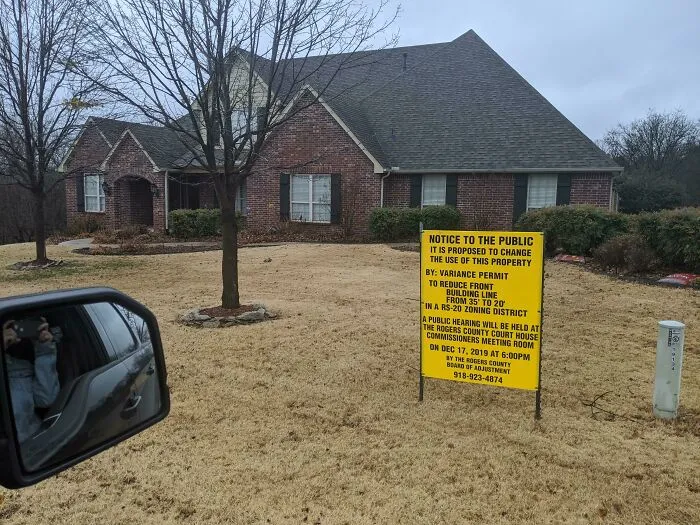 Yellow zoning notice sign posted on a lawn from infuriating neighbors in a residential area.