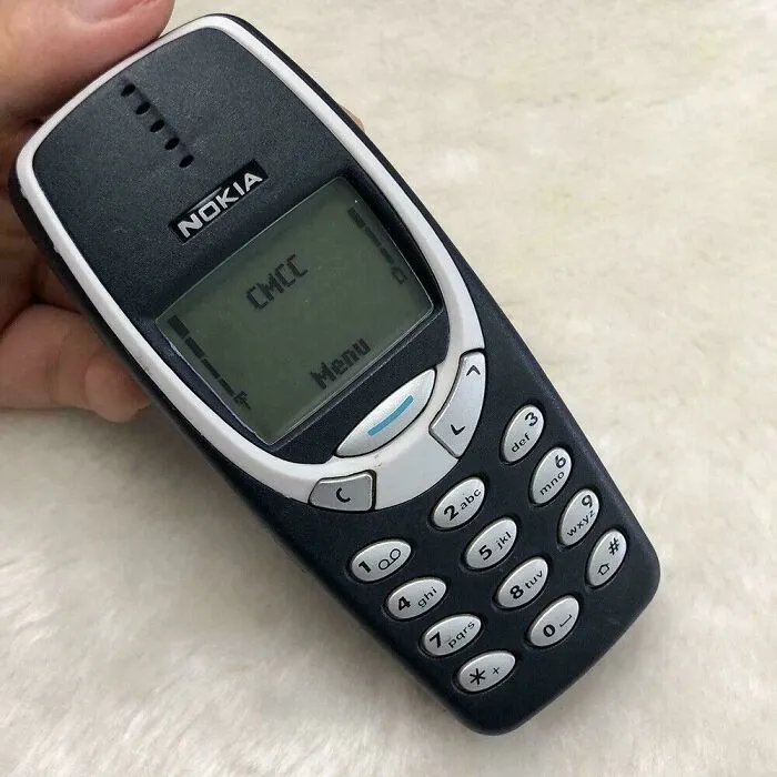 Classic dark grey Nokia 3310 cell phone held in hand from 2001.