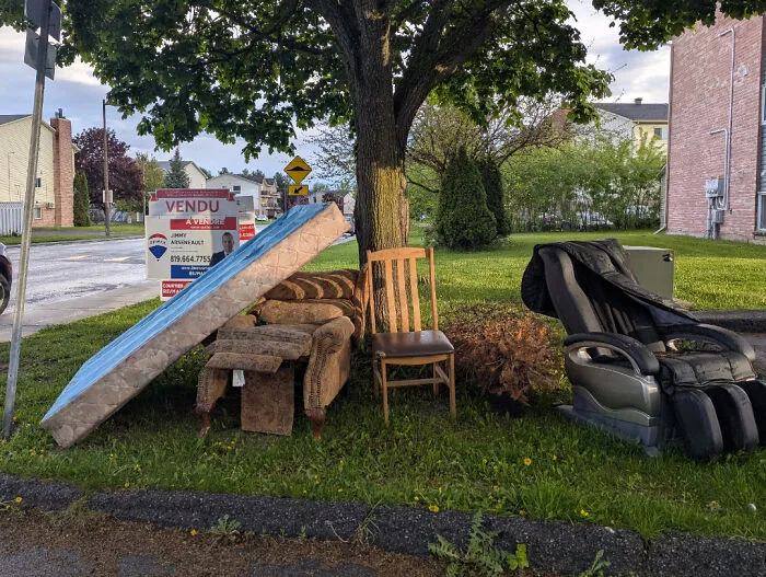 Old discarded furniture and mattress piled under a tree on the lawn by infuriating neighbors.