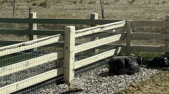 Light-colored wooden split rail fence with wire mesh from infuriating neighbors.