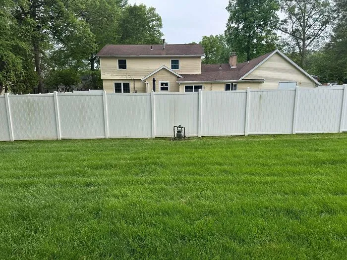A high white privacy fence built by infuriating neighbors enclosing a green suburban lawn.