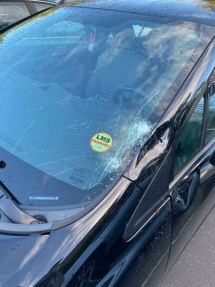 Car with cracked windshield and dented pillar showing damage caused by infuriating neighbors.