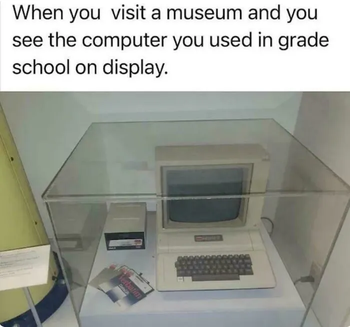 Early personal computer displayed in museum case with retro monitor and keyboard