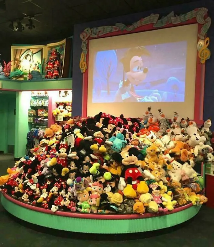 Large pile of Disney character plush toys with a movie screen backdrop nostalgic childhood photos