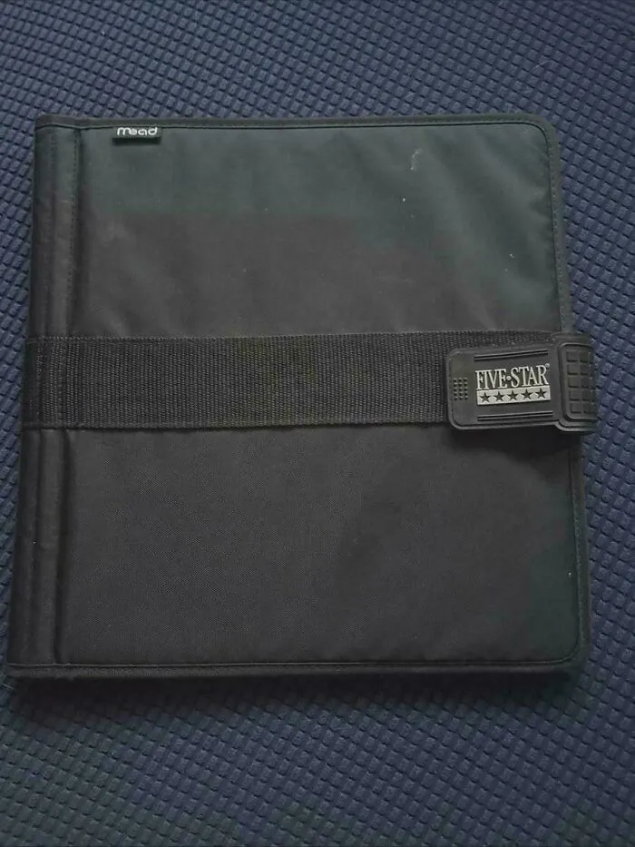 Black Five Star brand binder with a strap on a textured blue surface