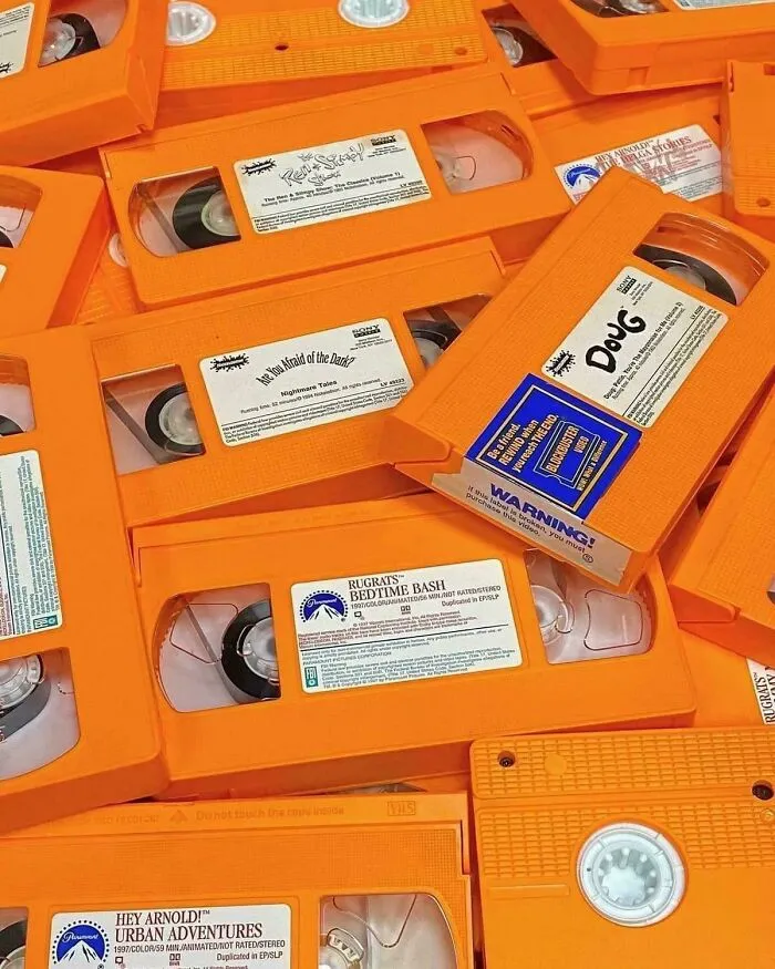 Orange VHS tapes of classic 90s cartoons like Doug and Rugrats piled together