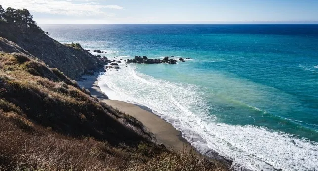 Scenic view of the blue ocean on the rocky West Coast of the United States with waves crashing on the beach.