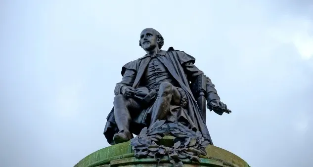 Bronze statue of William Shakespeare under a cloudy sky representing the author of Hamlet.