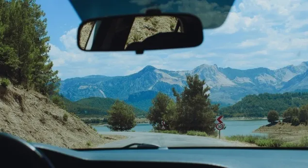 View from inside a car driving on a scenic road with mountains in the background