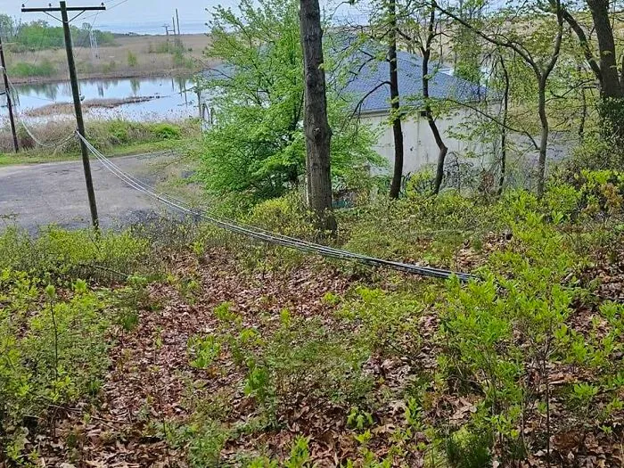 Utility pole cables lying across a grassy hill, an example of poor construction fails.
