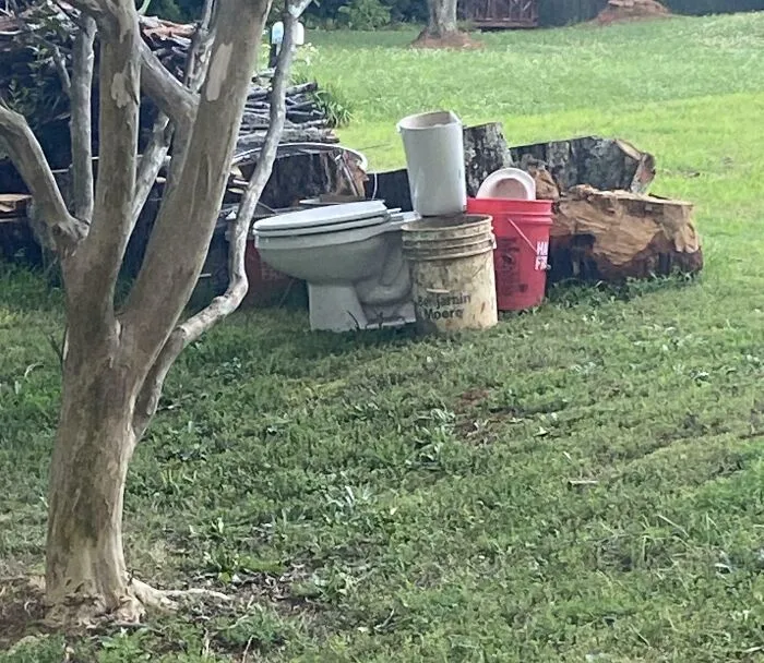 A white toilet and plastic buckets left sitting in an overgrown yard by infuriating neighbors
