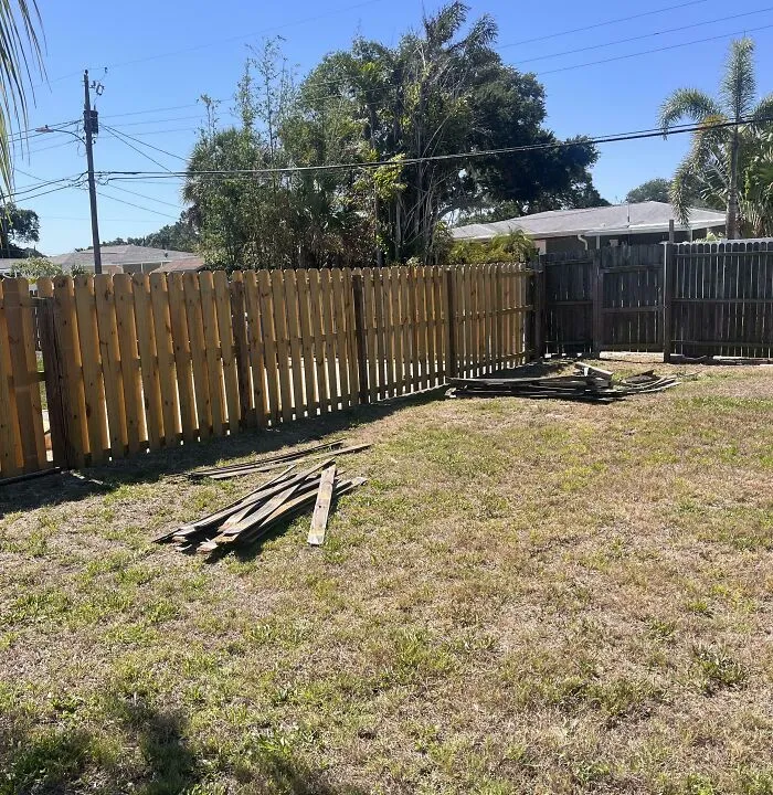 A newly installed wooden fence in a yard with piles of old fence boards left scattered by infuriating neighbors