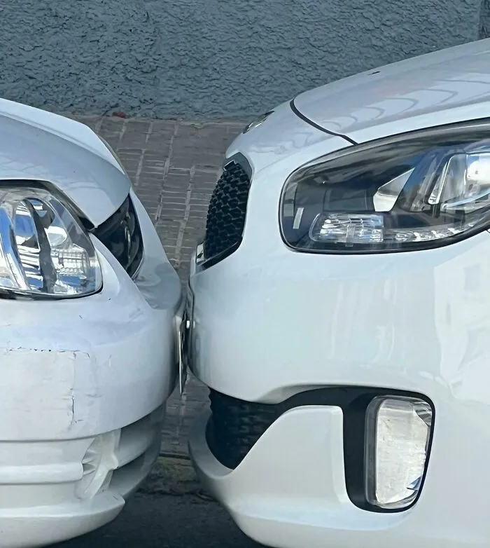 Close-up of two white cars parked extremely close together bumper to bumper by infuriating neighbors.
