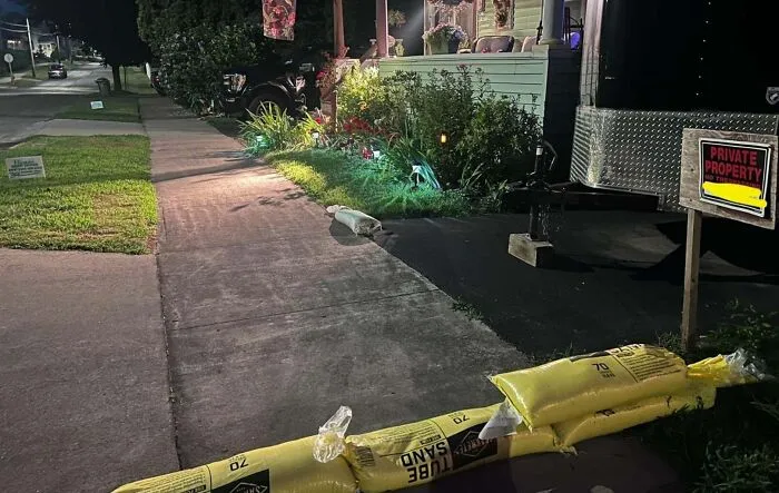 Infuriating neighbors sandbags blocking a sidewalk at night near a sign.