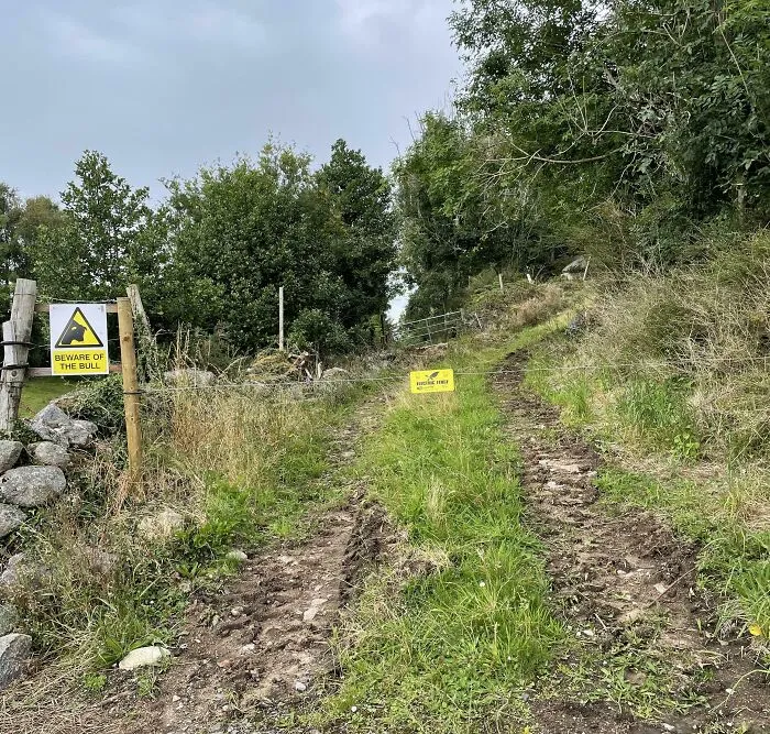 Electric wire fence blocking a path with a warning sign, caused by infuriating neighbors.