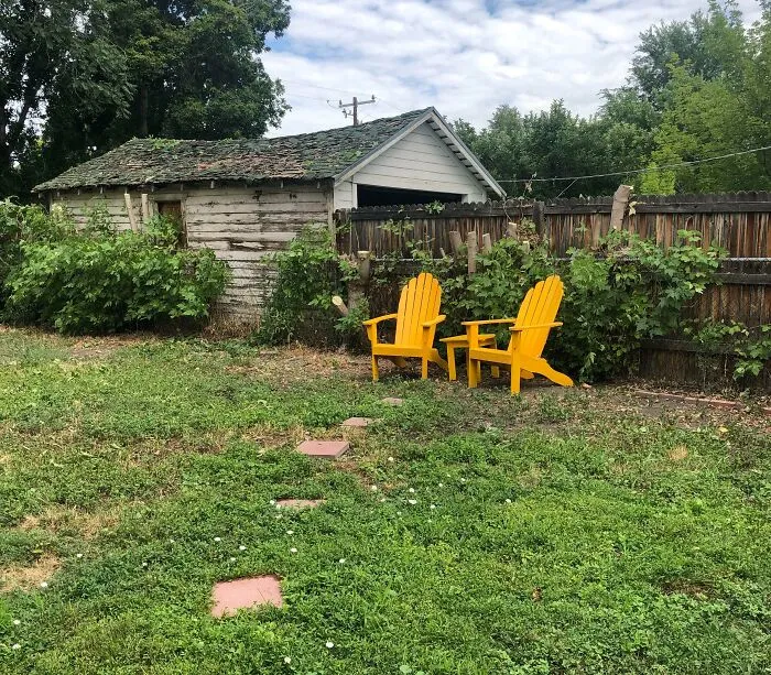 Overgrown backyard with yellow lawn chairs next to a wooden fence and shed, showcasing bad infuriating neighbors