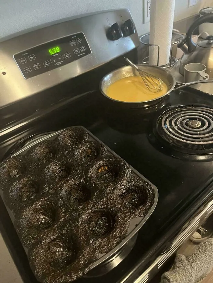 A major baking fail featuring completely burnt donuts in a donut pan on the stovetop.