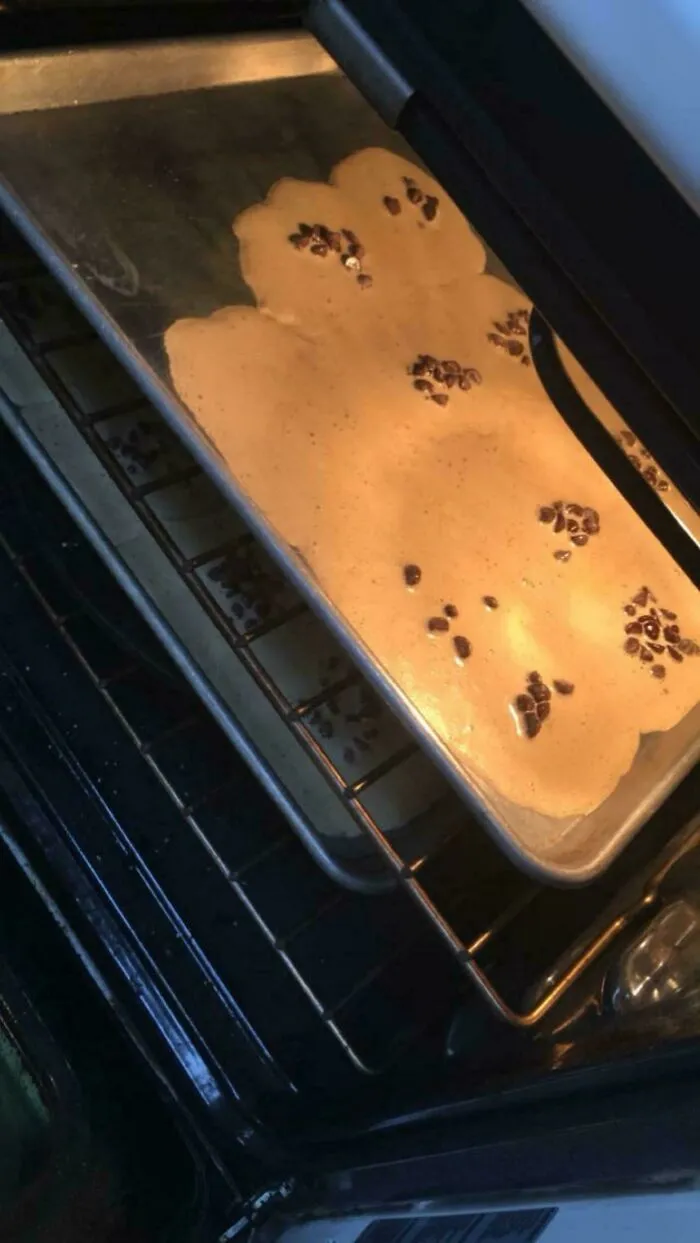 A baking fail with melted cookie dough spreading all over a baking sheet inside the oven.