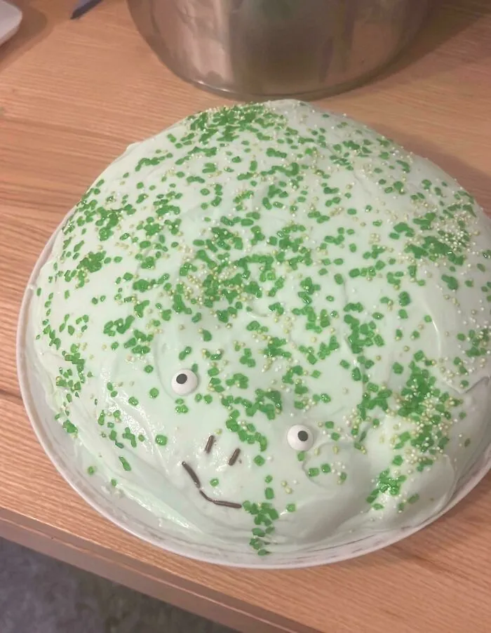 Cute baking fail frog cake with light green icing, candy eyes, and sprinkles.