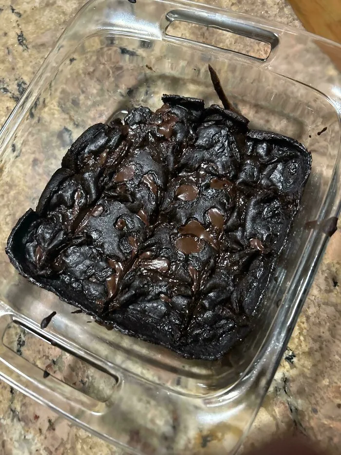 Overcooked, dark chocolate brownies in a square glass dish representing a baking fail.