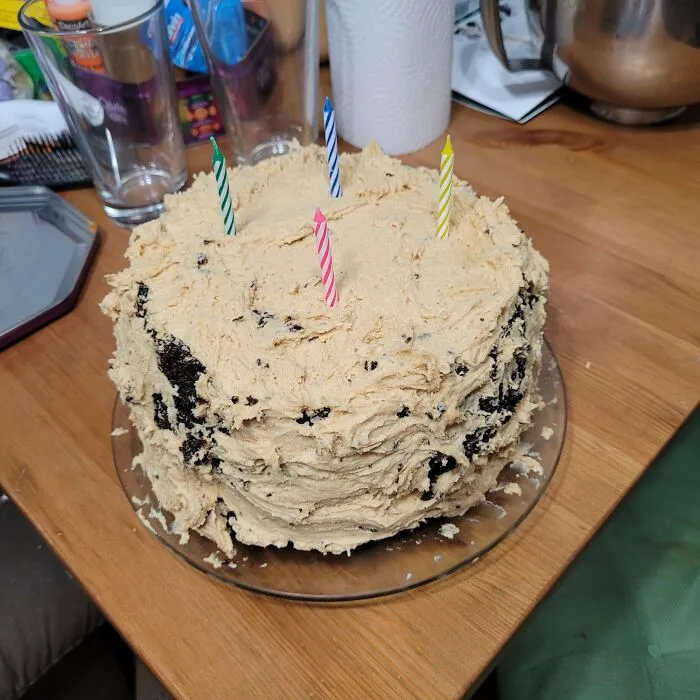 Homemade birthday cake with messy beige frosting and four candles, a humorous baking fail.