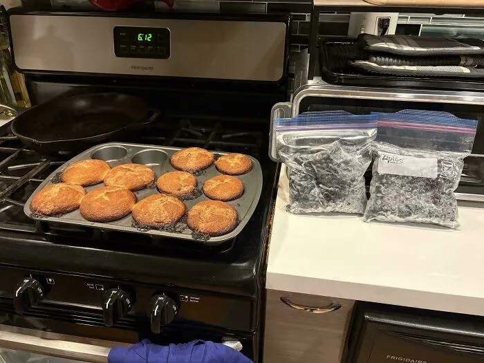 Pan of muffins on a stove near frozen blueberries showing a baking fail