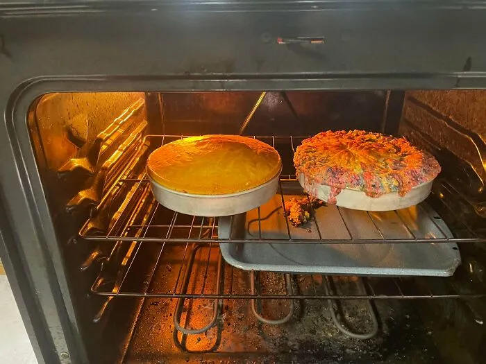 Two cake pans inside an oven, one overflowing into a baking fail mess.