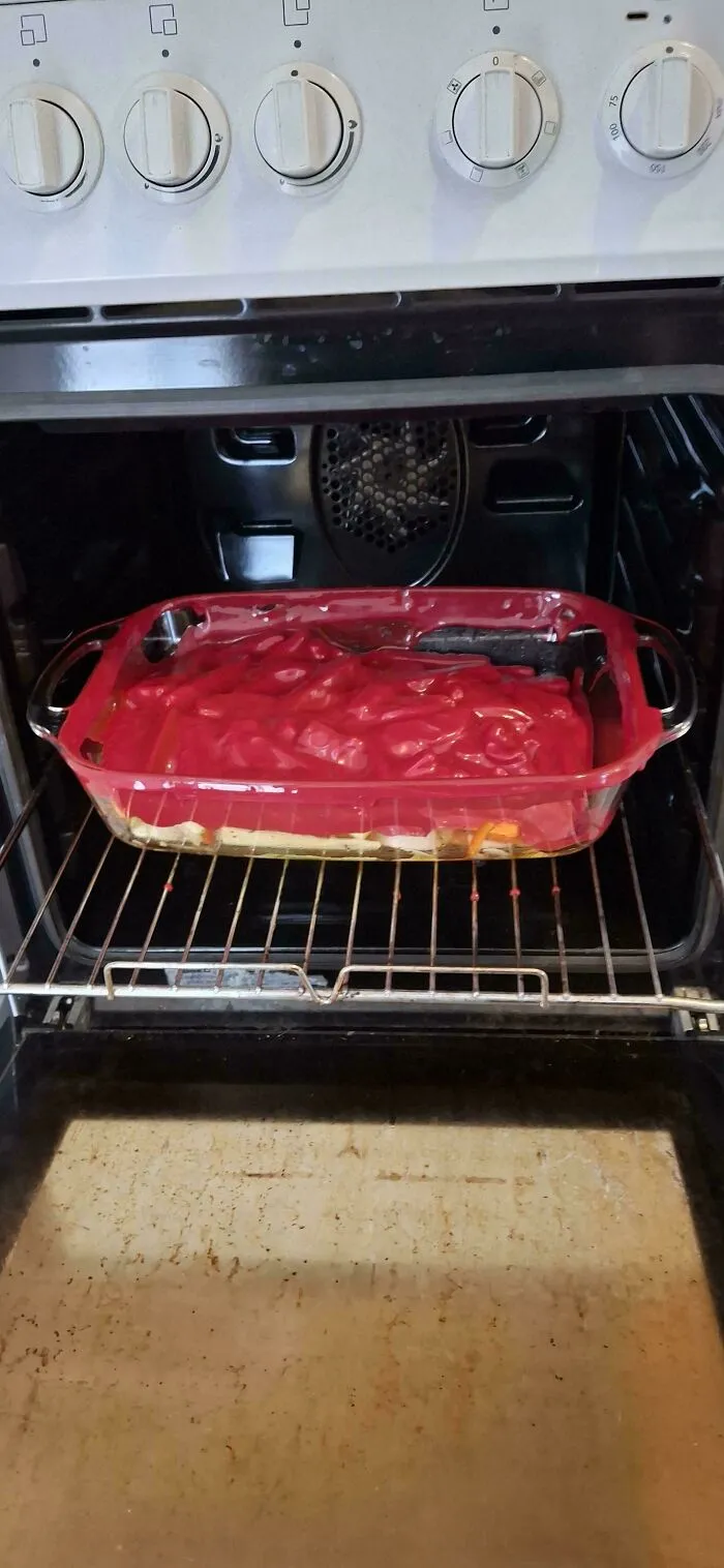 A baking fail with a melted red plastic lid inside a hot oven covering a casserole.