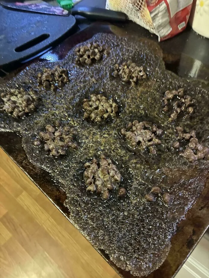 Completely melted burnt cookies spread over a baking sheet in a major baking fail.