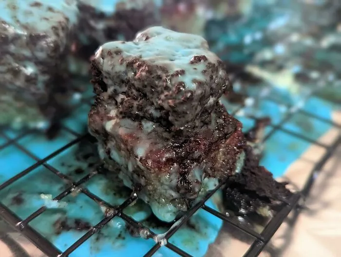 Messy chocolate brownies covered in light blue glaze resting on a wire rack, a classic r/bakingfail moment.